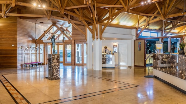 A spacious lobby with a high wooden ceiling, a reception desk, and a marble pillar.