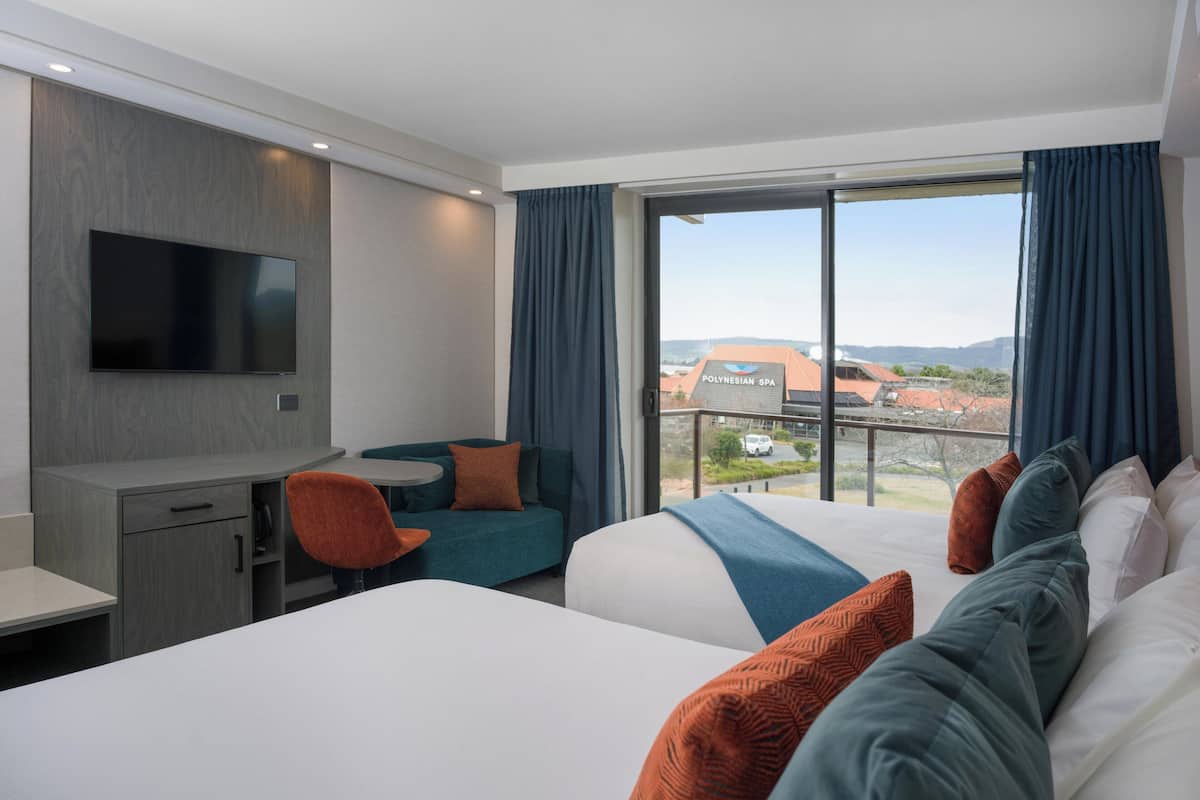 A hotel room with a bed, a desk, a chair, and a TV. There is a window with a view of a building outside.