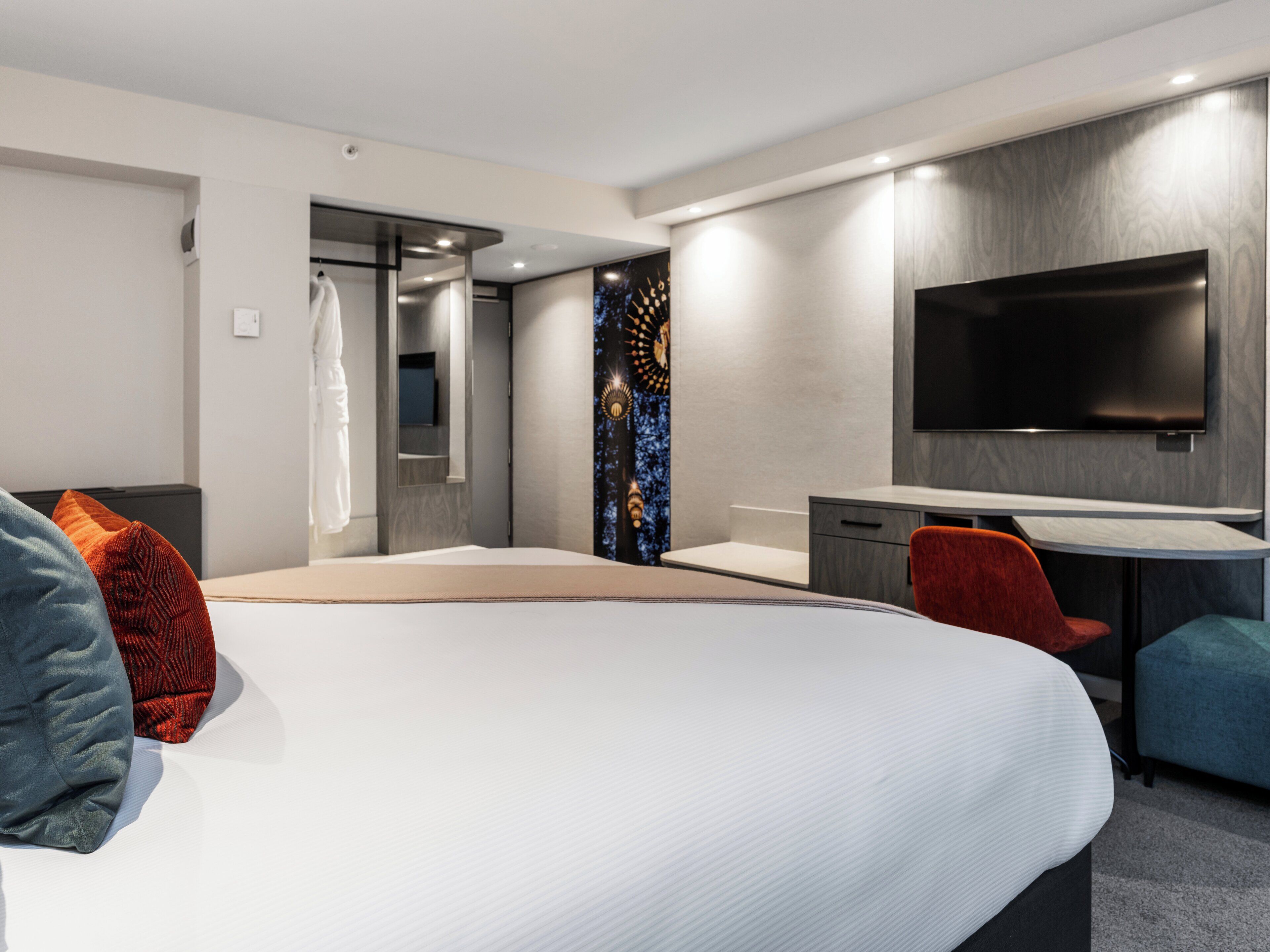 Et moderne hotelværelse med en stor seng, et skrivebord, et fladskærms-tv og et garderobeskab.