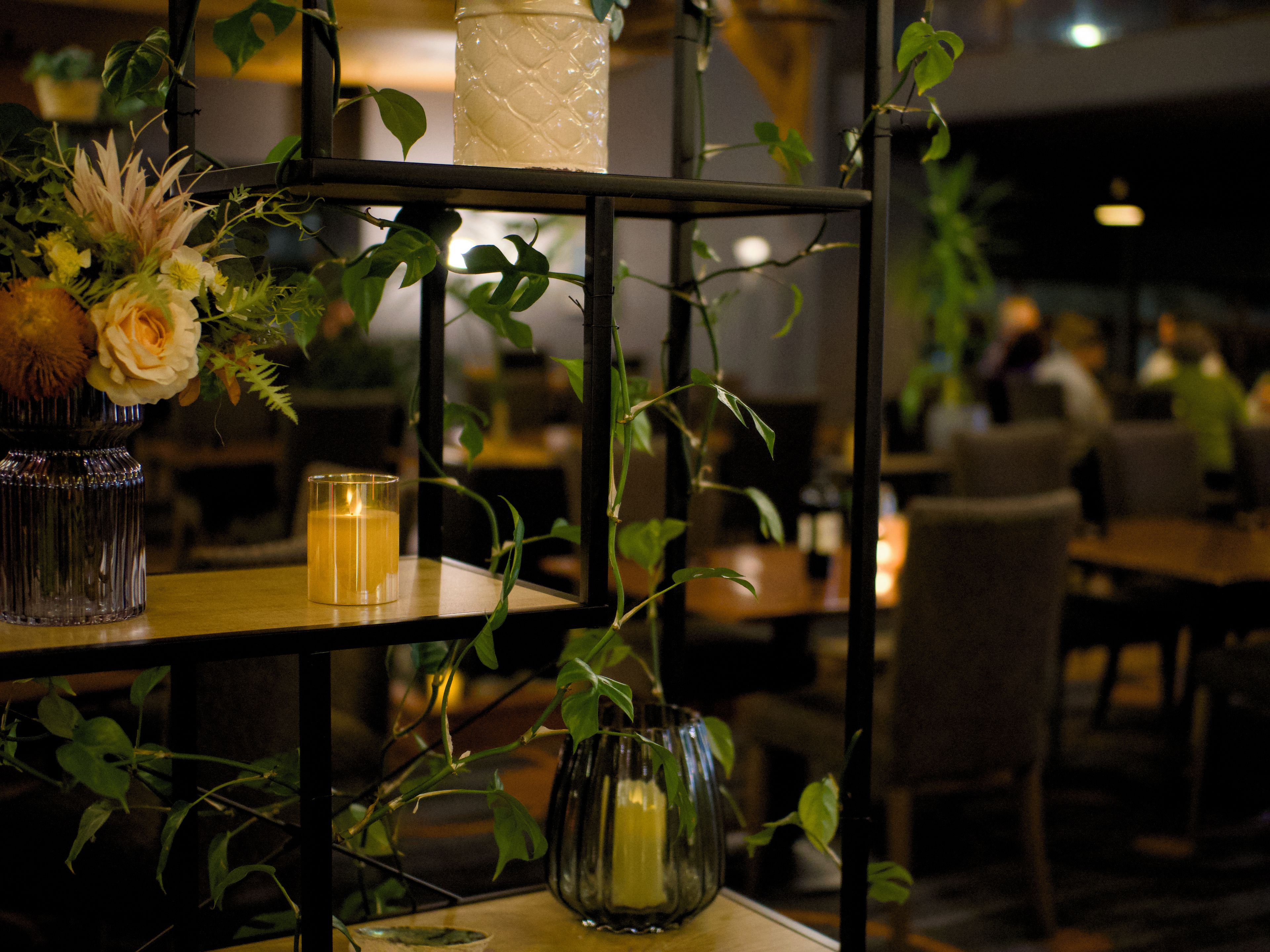 A shelf with vases and candles, surrounded by greenery.