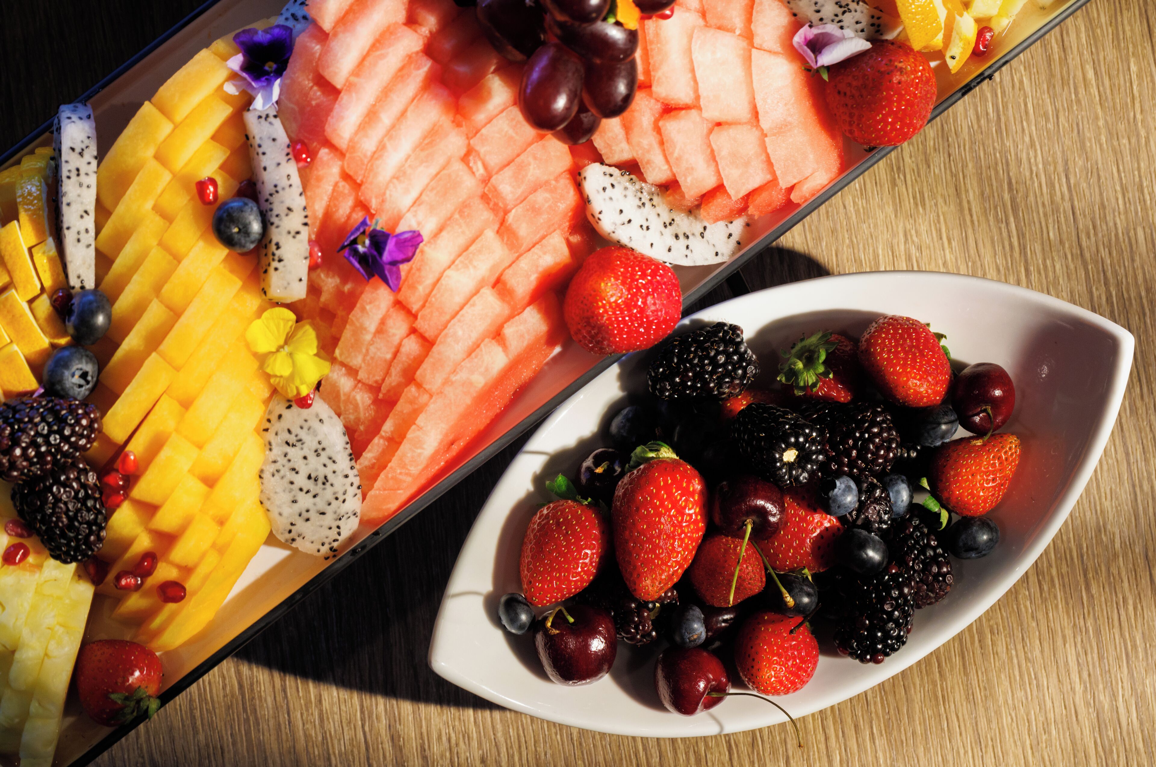 Una bandeja de frutas con diversas frutas y un tazón de bayas mezcladas.