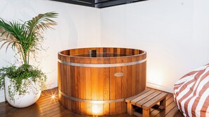 A wooden hot tub with a bench and a potted plant in a corner.