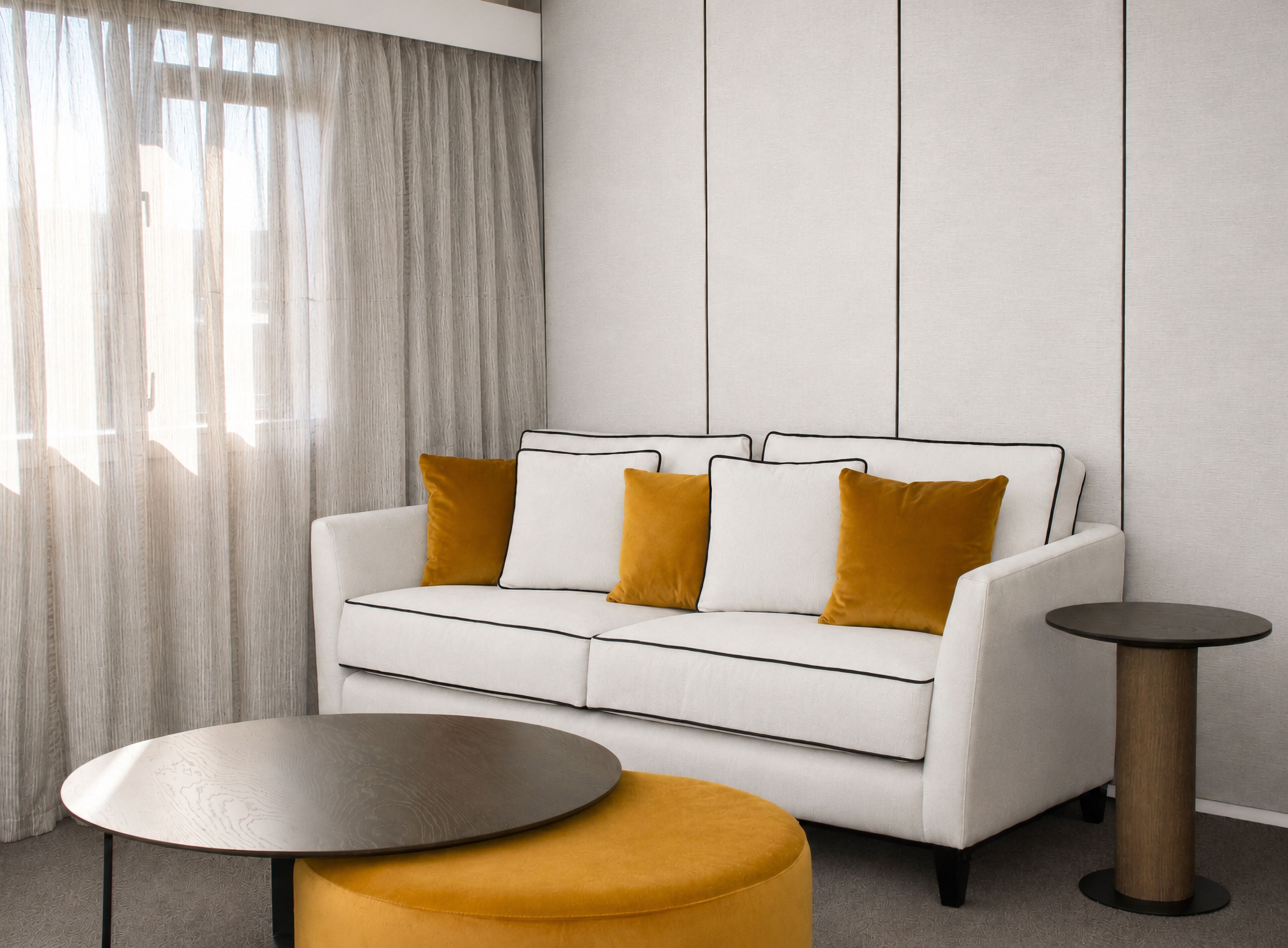 A modern living room with a white sofa, mustard-colored cushions, a round coffee table, and a side table.