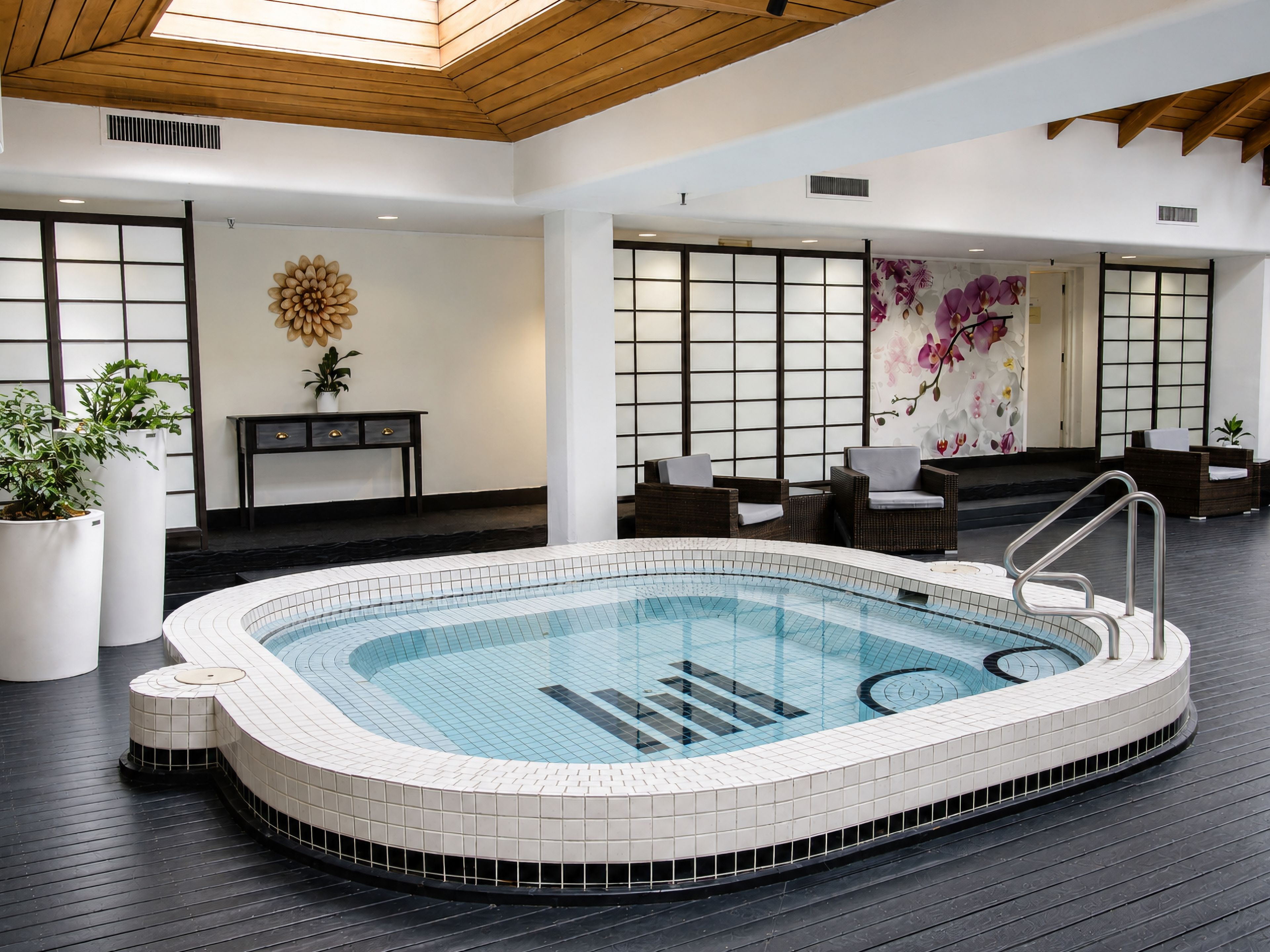 Piscina interior moderna com borda azulejada, rodeada por soalho de madeira escura e áreas de estar mobiliadas.