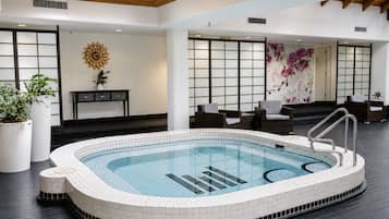 Piscina interior moderna com borda azulejada, rodeada por soalho de madeira escura e áreas de estar mobiliadas.