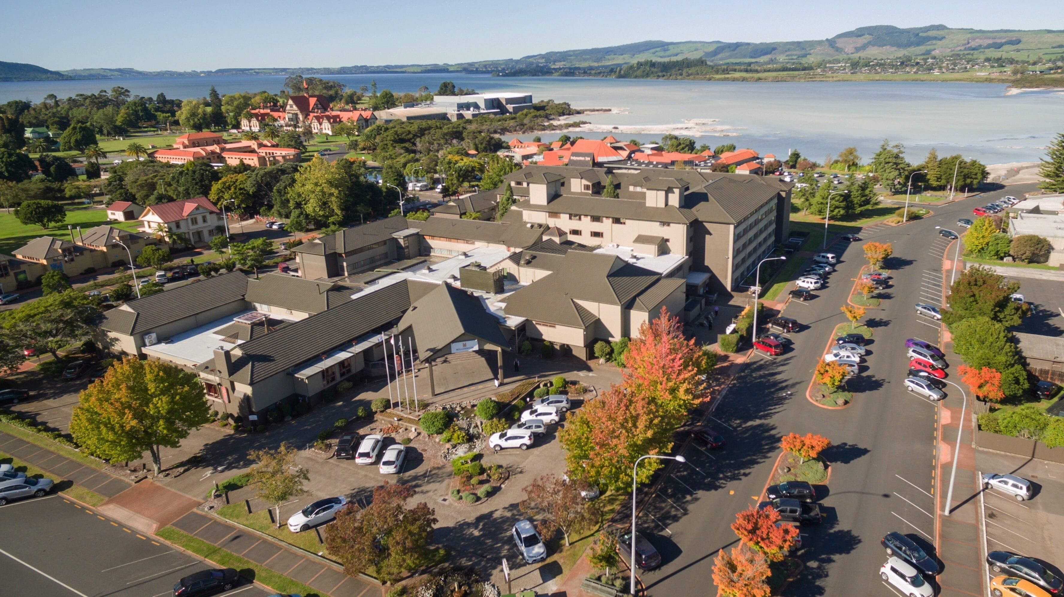 An aerial view of a residential area with a large building complex, parking lots, and a body of water in the background.