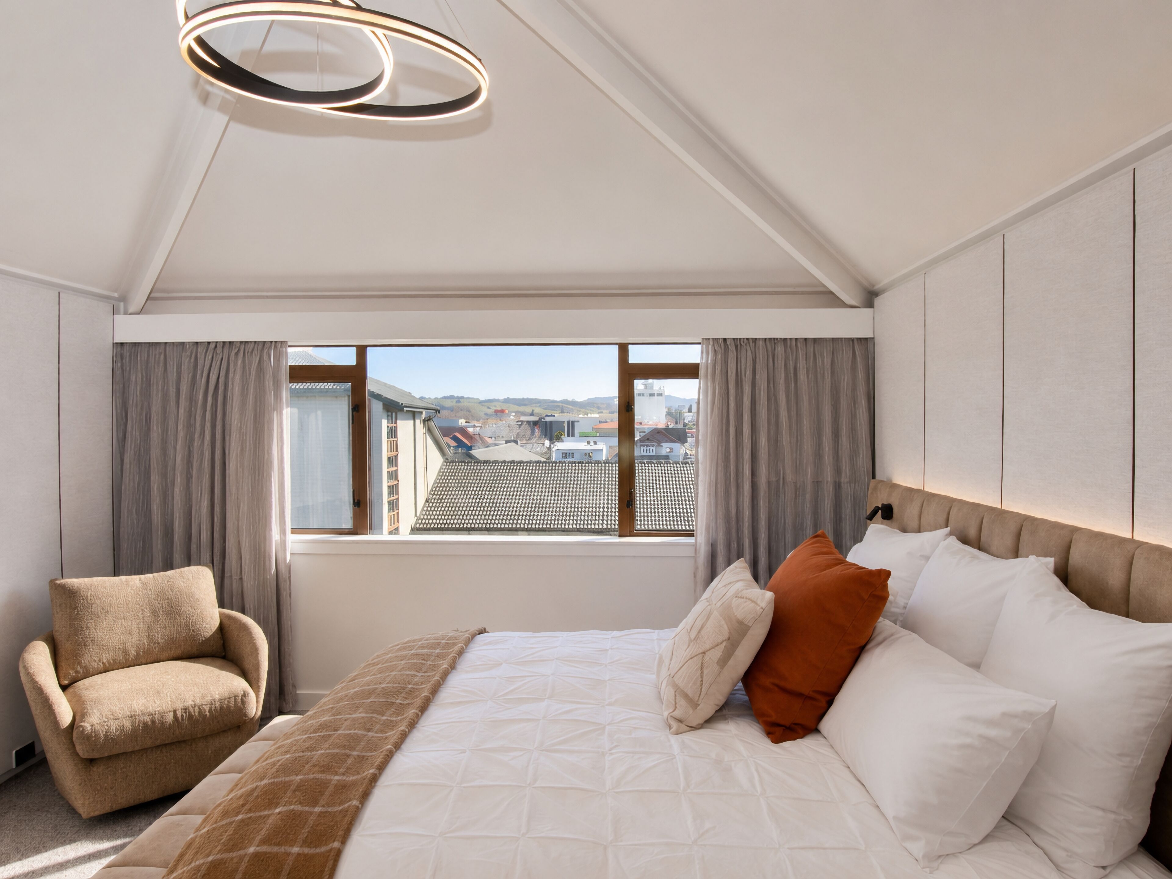 Une chambre d’hôtel avec un lit, une chaise, une fenêtre avec des rideaux et une vue sur des immeubles.
