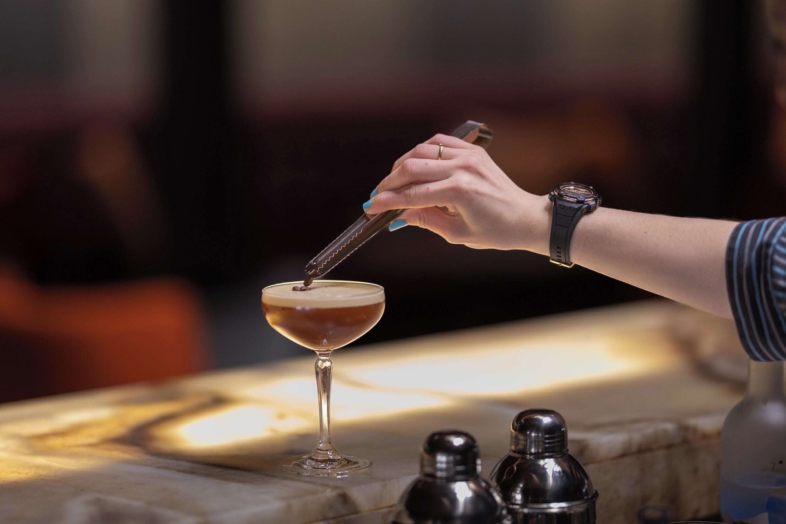A hand pouring a drink into a martini glass on a bar counter.