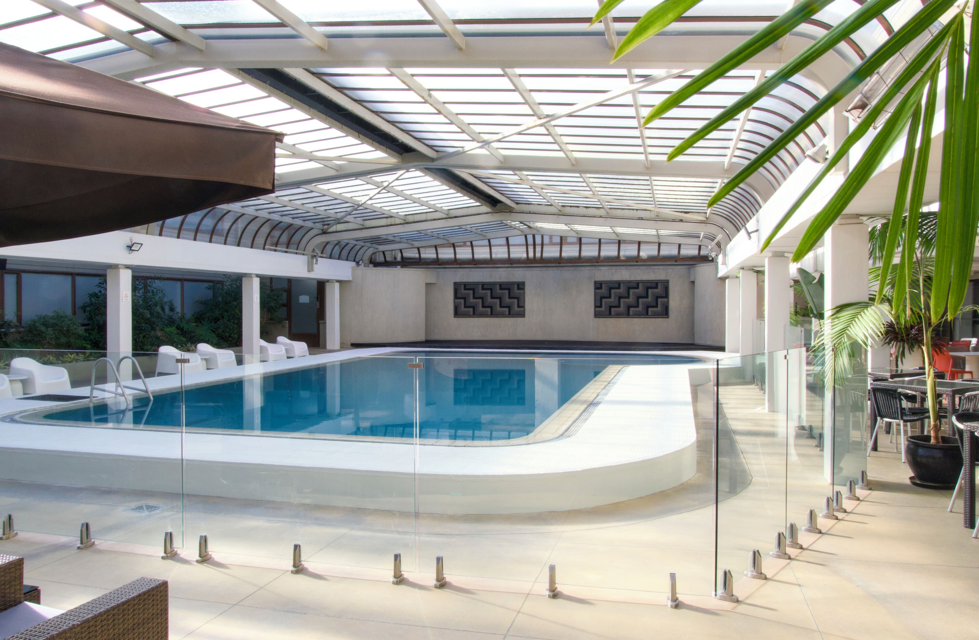 Une piscine intérieure dotée d’une paroi vitrée, entourée de chaises longues et de tables.