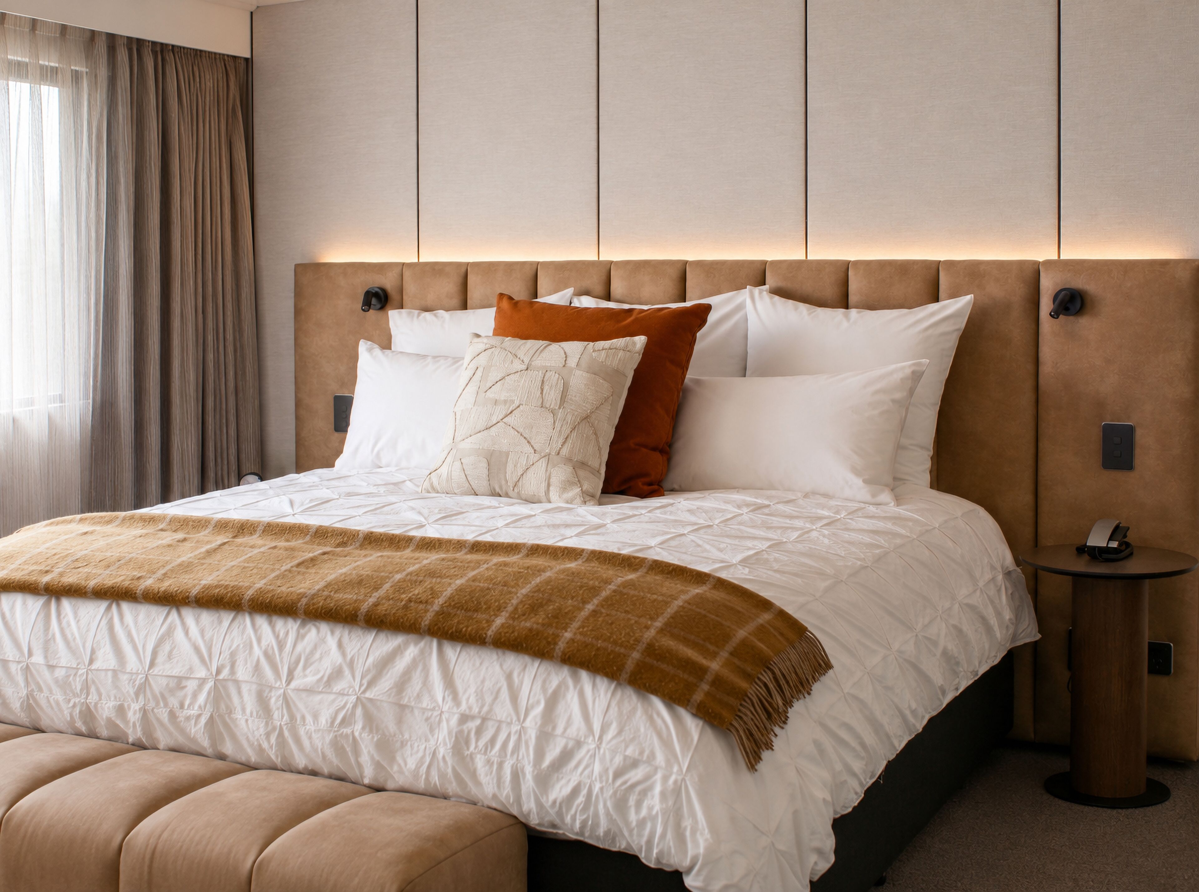 A hotel room with a large bed, a bedside table, and a headboard with built-in lighting.