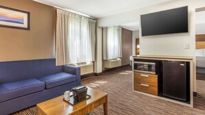 A hotel room with a sofa, a small table, a flat-screen TV, a mini-fridge, and a microwave. - Quality Inn Asheboro South (Asheboro)