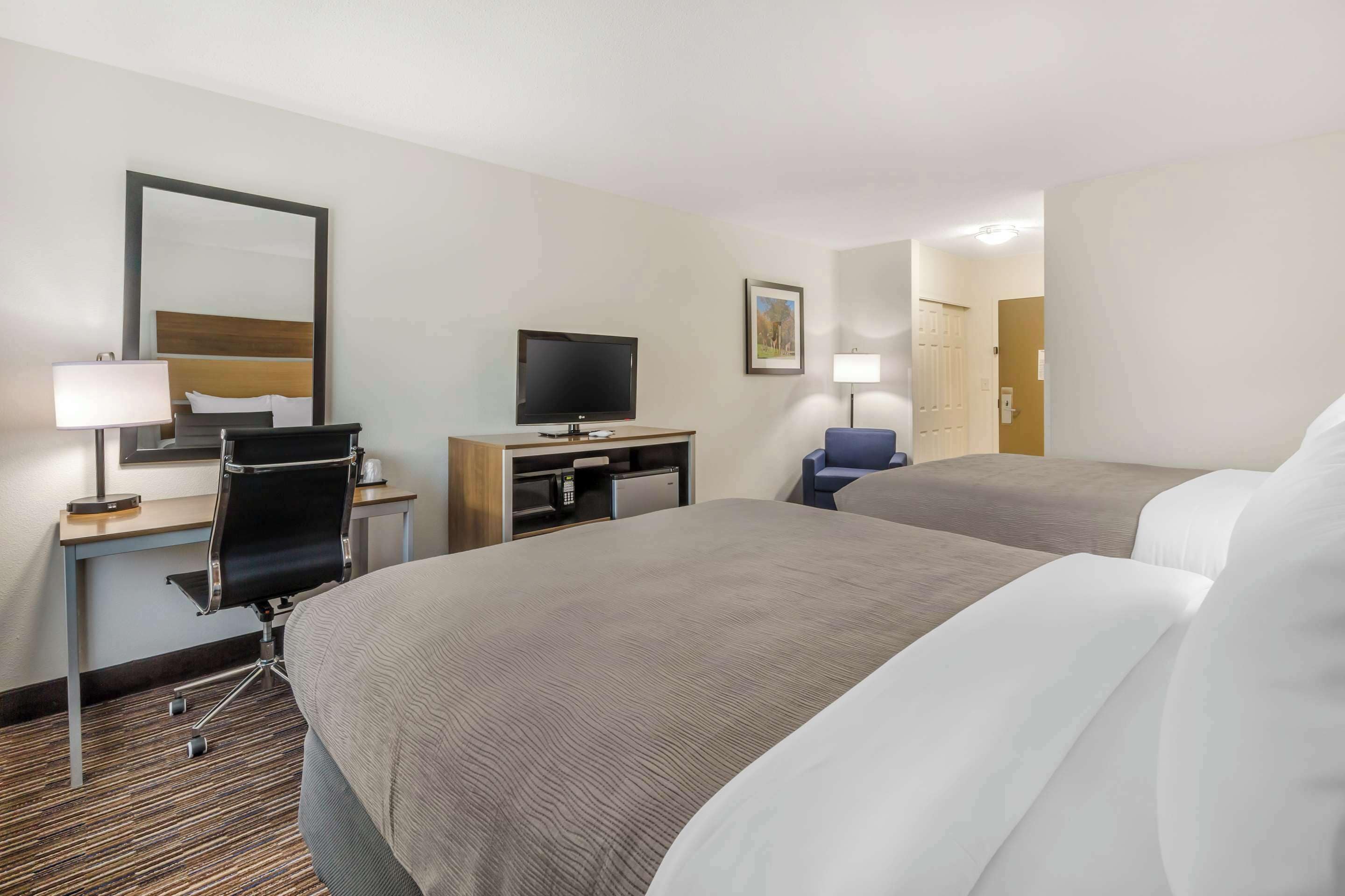 A hotel room with two beds, a desk with a computer, a television, and a small kitchenette.