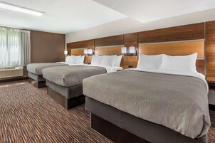Habitación de hotel con dos camas, un ventanal grande con cortinas, cabecera de madera y alfombra estampada.