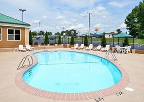 Una piscina con borde de ladrillo, rodeada de sillas de descanso y una zona cubierta.