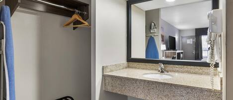 A bathroom with a sink, mirror, towel rack, and a shower area.