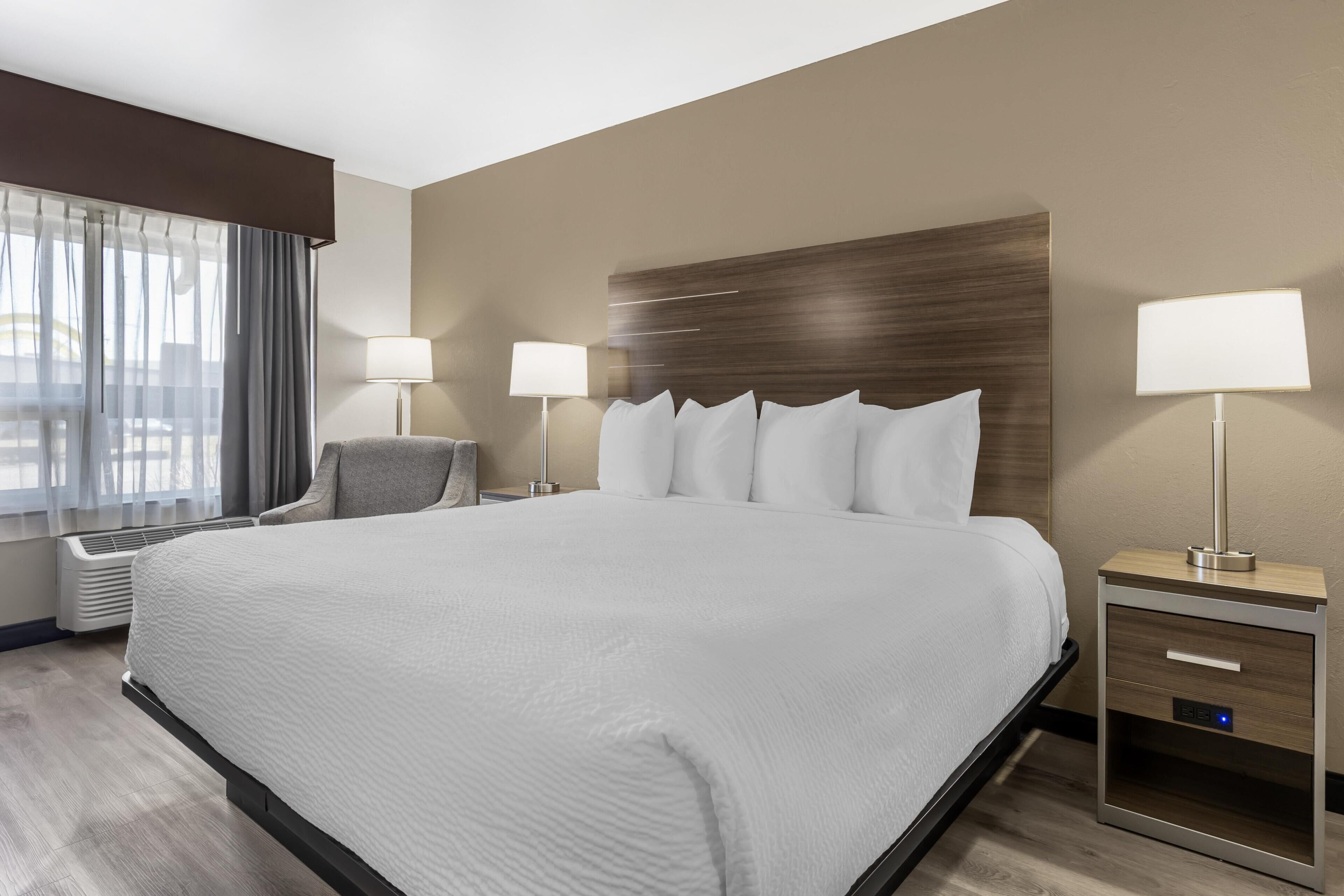 Een hotelkamer met een groot bed, nachtkastjes met lampen, een stoel en een raam met gordijnen.