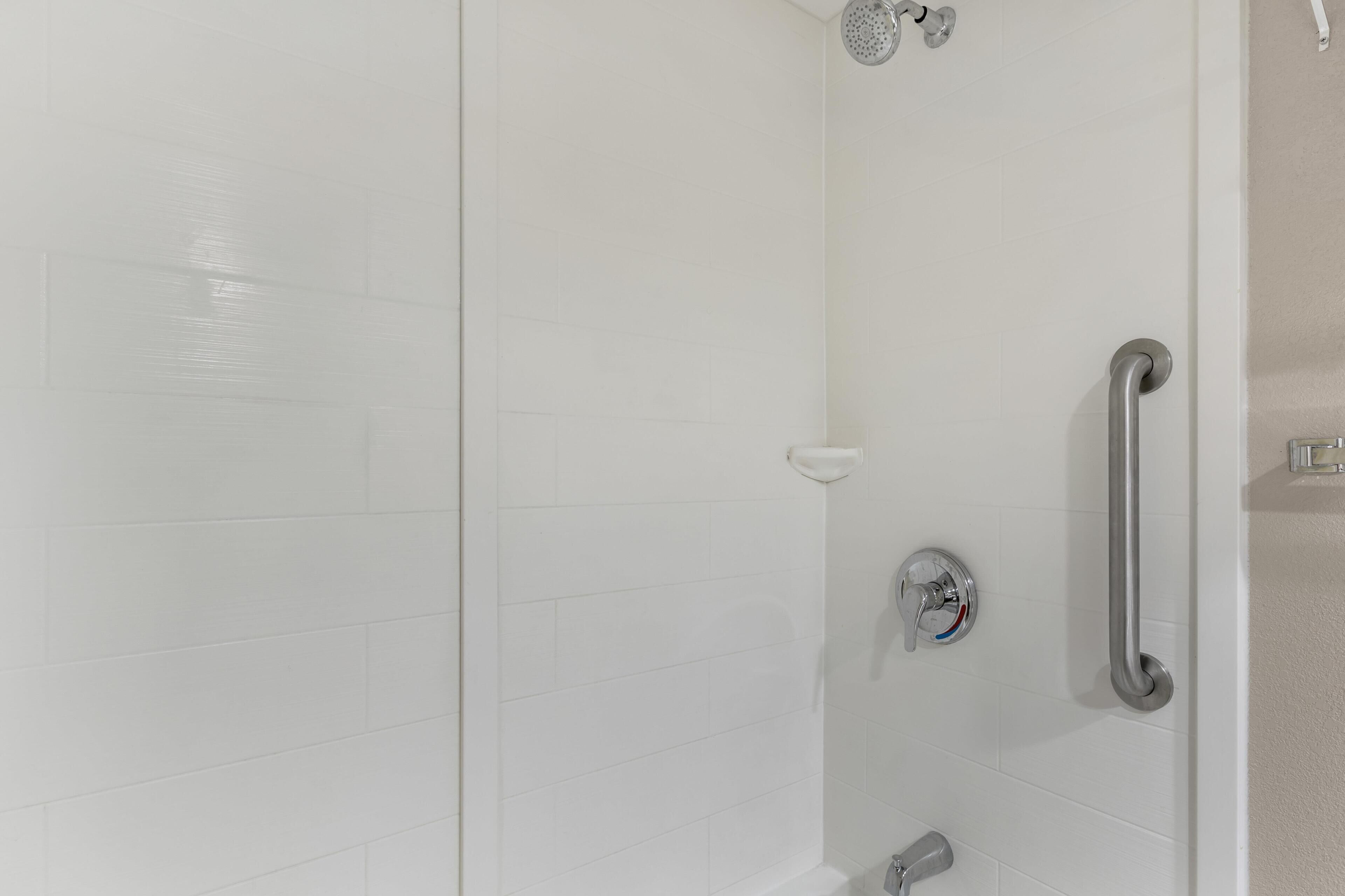 Une douche équipée d’un pommeau de douche à main, d’une barre d’appui mobile et d  ’un robinet mural.