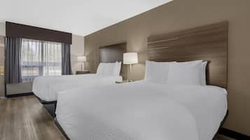 Quarto de hotel com duas camas, uma janela com cortinas, uma mesa de cabeceira com abajur e cabeceira de madeira.