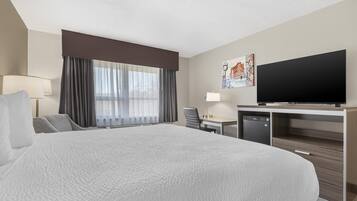A hotel room with a large bed, a desk, a television, and a window with curtains.
