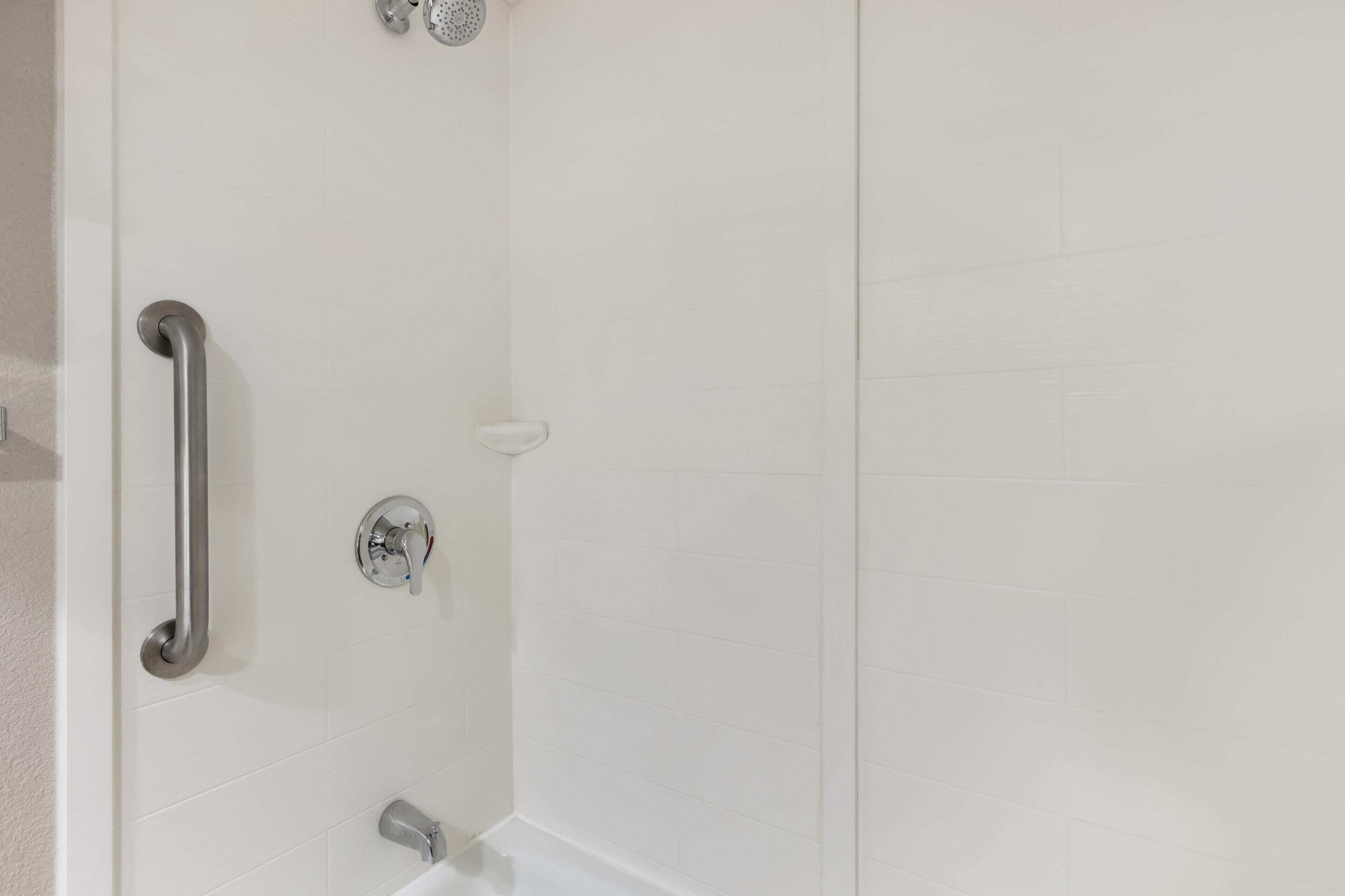 Une douche équipée d’une barre d’appui, d’un pommeau de douche à main et de commandes fixées au mur.