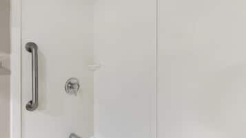 A shower with a handrail, a handheld showerhead, and a wall-mounted control.