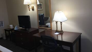 A hotel room with a desk, two lamps, a television, a mirror, and a chair.