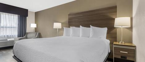 Una habitación de hotel con una cama grande, dos lámparas de noche, una silla y un ventanal con cortinas.