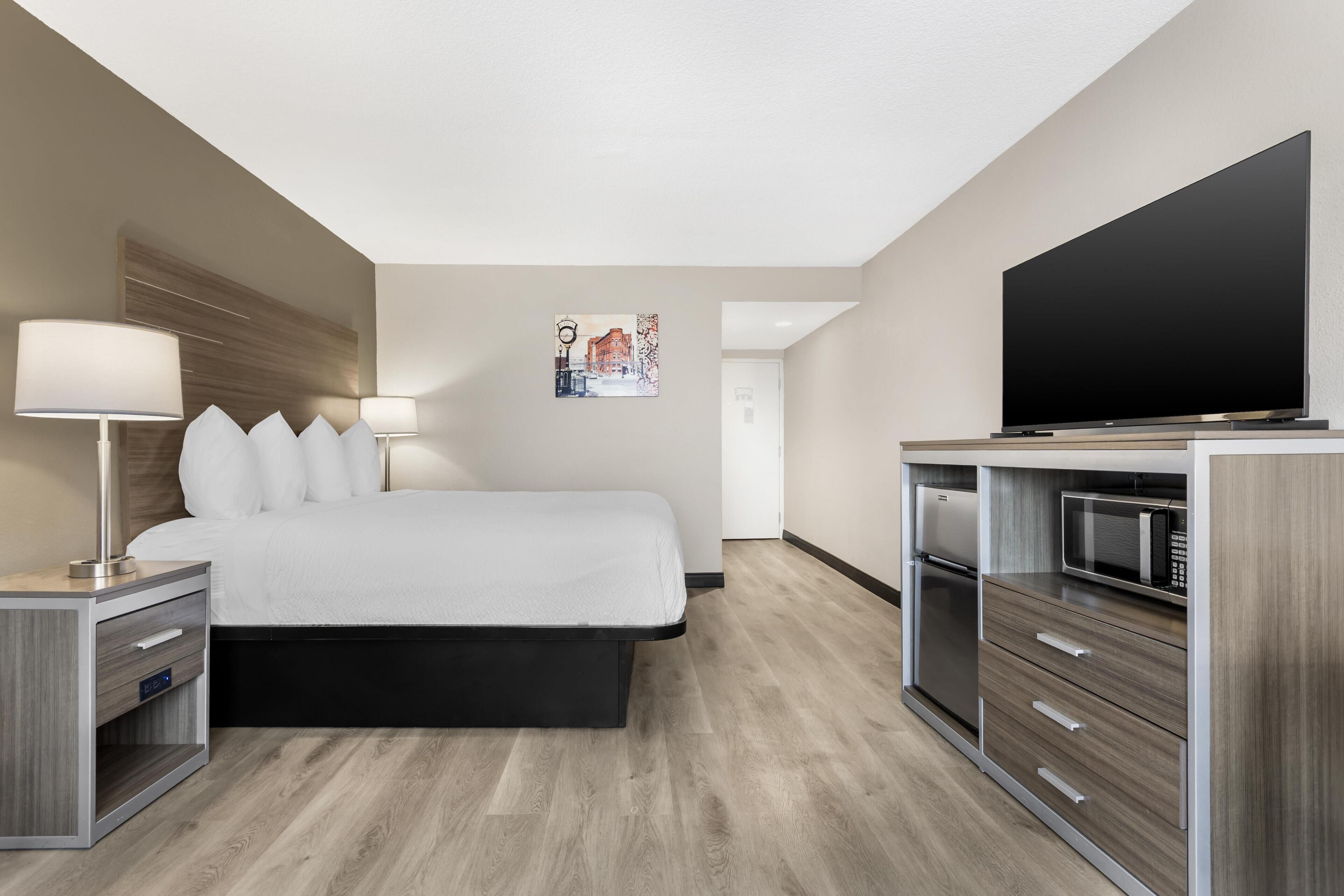 Een hotelkamer met een bed, nachtlampjes, een flatscreen televisie, een magnetron en een koelkast.