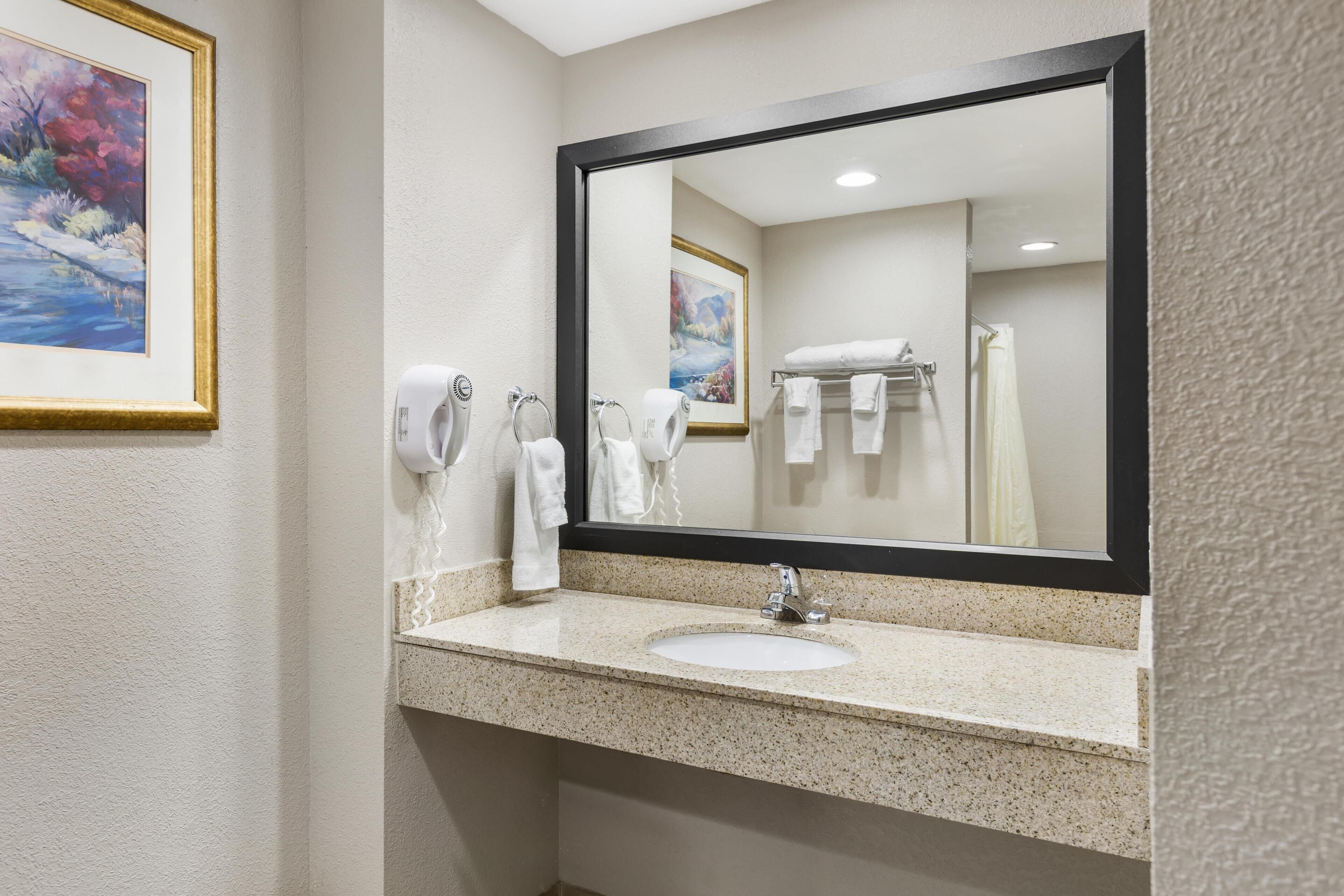 A bathroom with a sink, mirror, towel dispenser, and a framed painting on the wall.