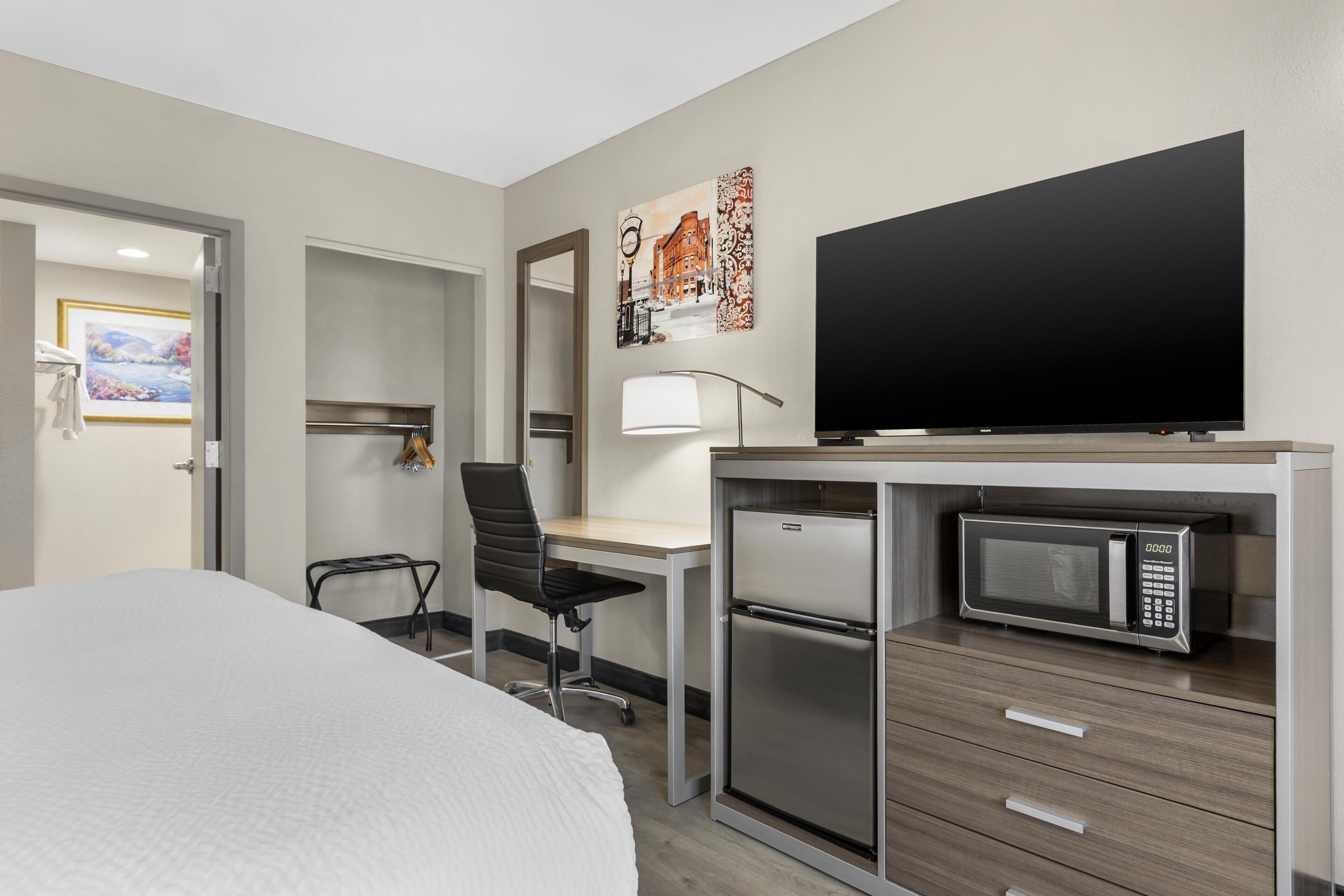 Een hotelkamer met een bed, bureau, stoel, televisie, magnetron en een kleine koelkast.