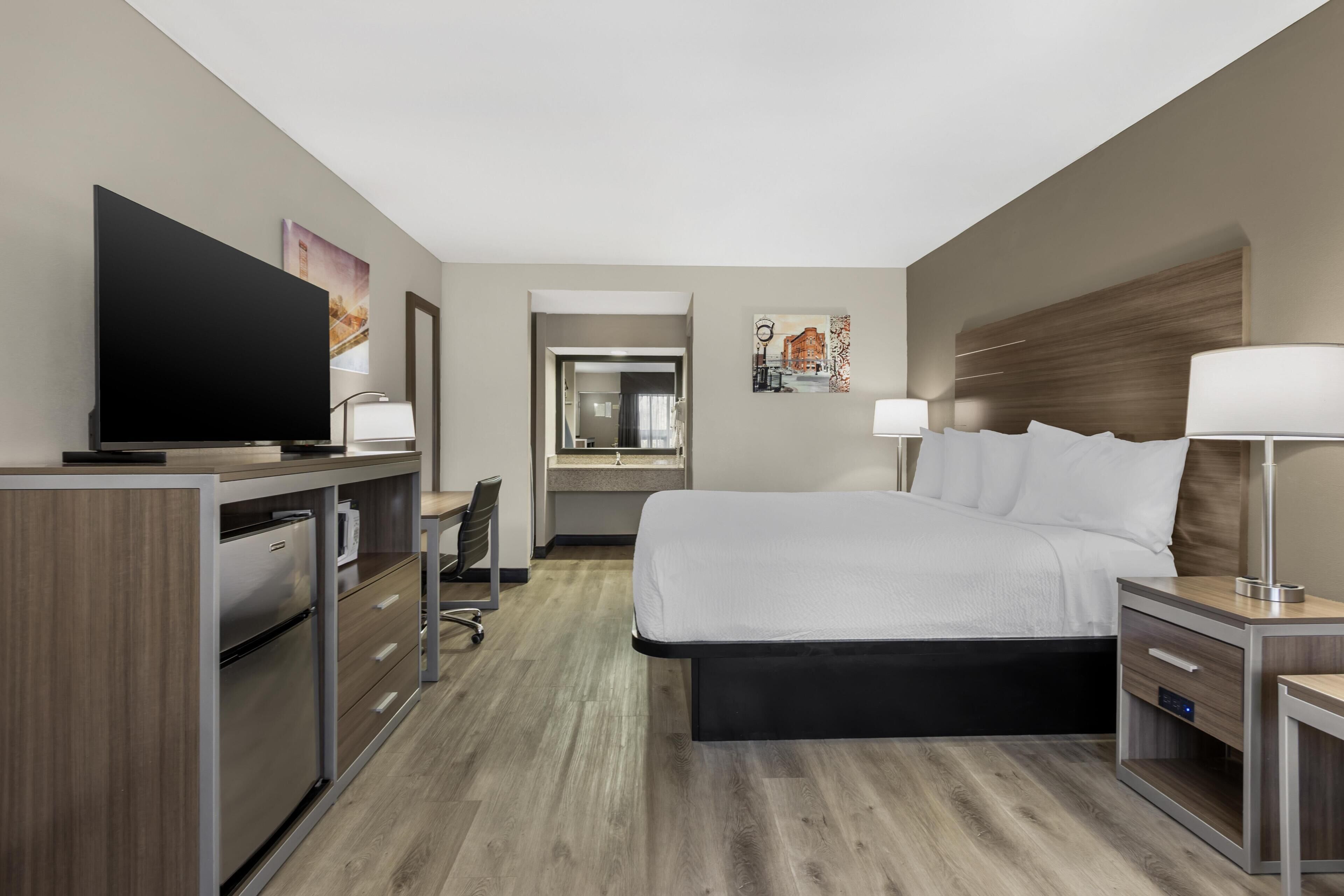 A hotel room with a bed, desk, TV, and a view of the city.