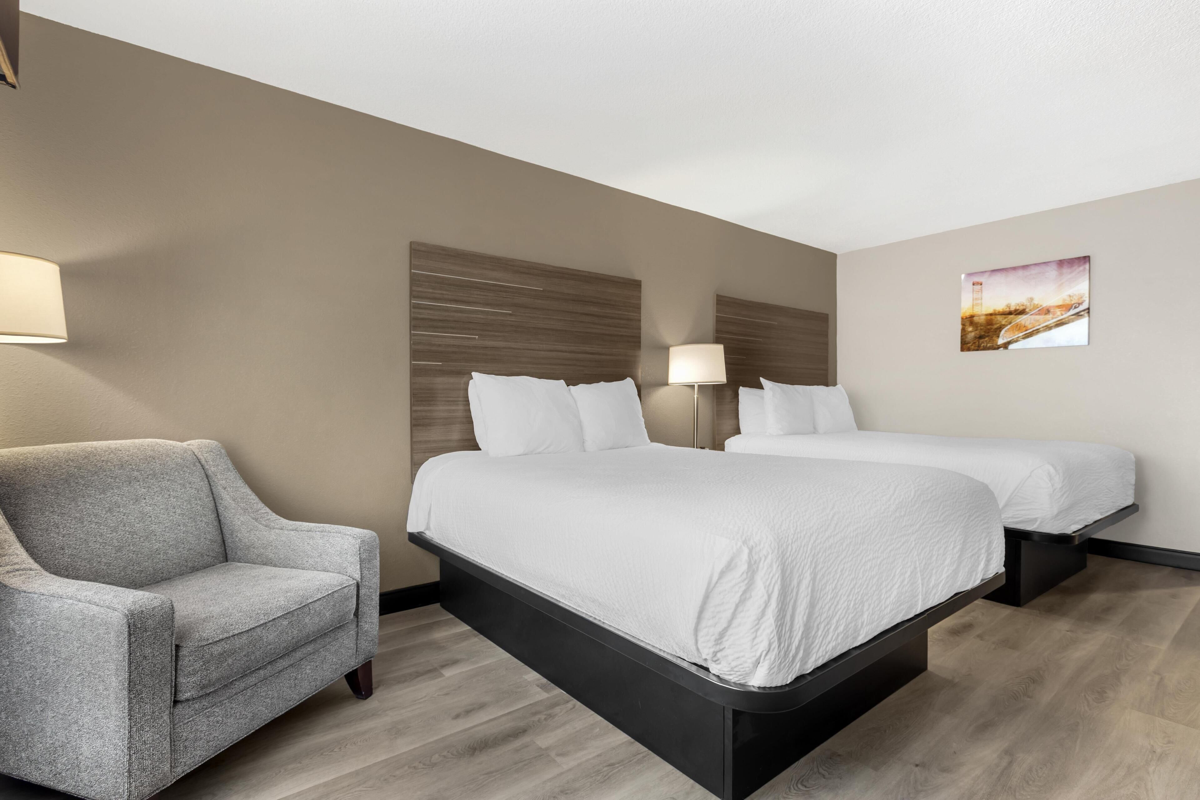 Een hotelkamer met een bank, twee bedden, een hoofdeinde, een lamp en een foto aan de muur.