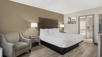 A hotel room with a bed, a chair, a nightstand, a lamp, and a painting on the wall.
