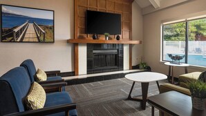 Een woonkamer met een open haard, een televisie erboven en een groot raam met uitzicht op een zwembad.