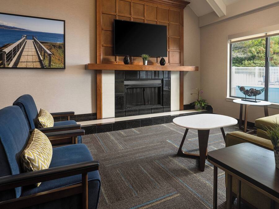 A living room with a fireplace, a television mounted above it, and a large window overlooking a pool.