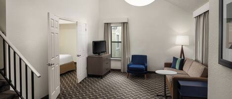 A hotel room with a bed, a desk, a chair, a sofa, a TV, and a staircase.