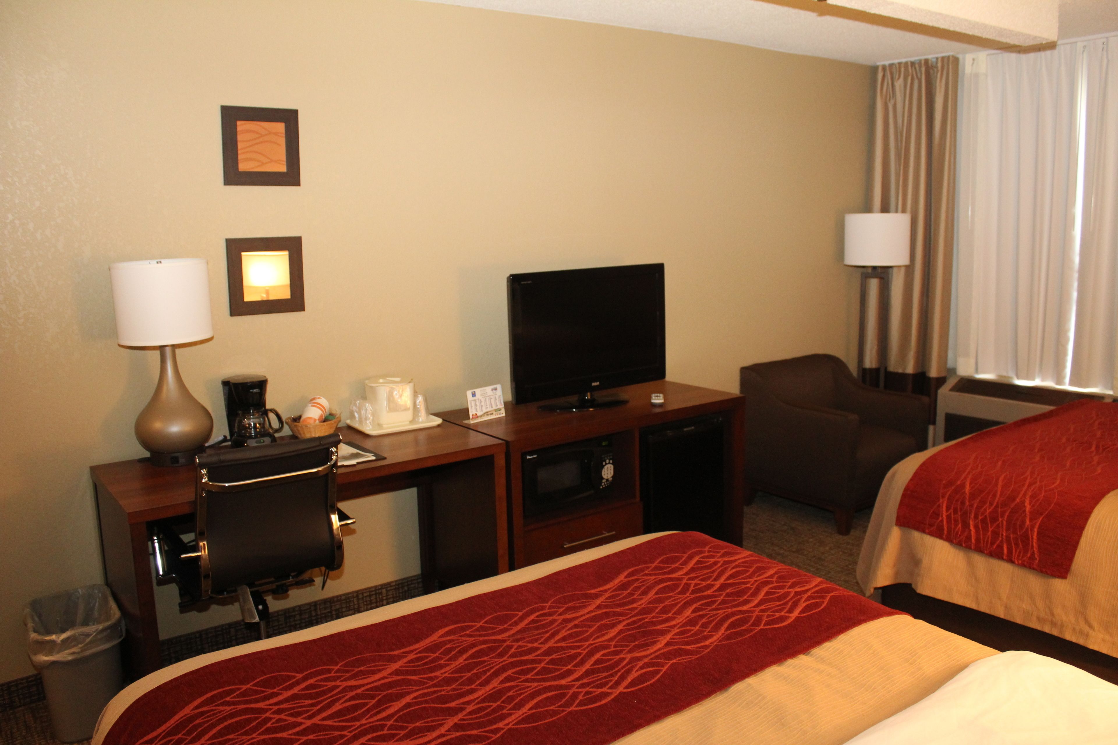 Habitación de hotel con escritorio, televisión, dos camas, una silla y un cesto de basura.
