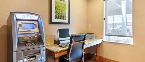 Un cajero automático, una computadora de escritorio y una silla en una habitación con suelo de madera y una ventana.