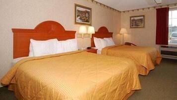 A hotel room with two beds, each with a headboard and bedside lamps.