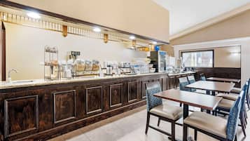 A hotel breakfast area with a buffet counter, seating, and a large window.