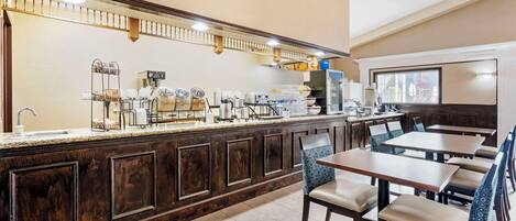 A hotel breakfast area with a buffet counter, seating, and a large window.
