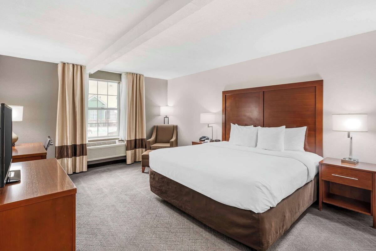 A hotel room with a large bed, a desk, a chair, a TV, and a window with curtains.