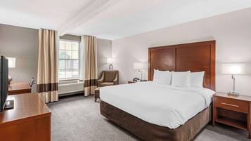 A hotel room with a large bed, a desk, a chair, a TV, and a window with curtains.