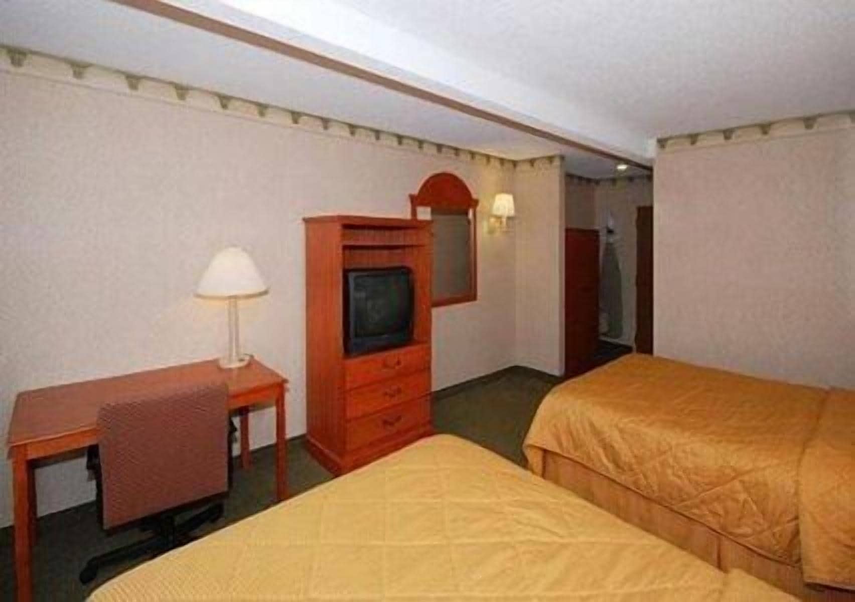 Camera d'albergo con due letti, una scrivania con lampada, una televisione e uno specchio.