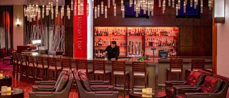 Zona de bar con asientos de cuero, un barman y una estantería bien surtida de licores.
