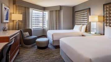 Ein Hotelzimmer mit zwei Betten, einem Schreibtisch, einem Stuhl und einem großen Fenster mit Vorhängen.