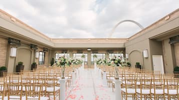 An indoor venue with rows of wooden chairs and white cushions, arranged in a semi-circular aisle with a white floor.