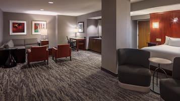 A hotel room with a bed, two armchairs, a small table, a desk with a chair, a sofa, and a carpeted floor.