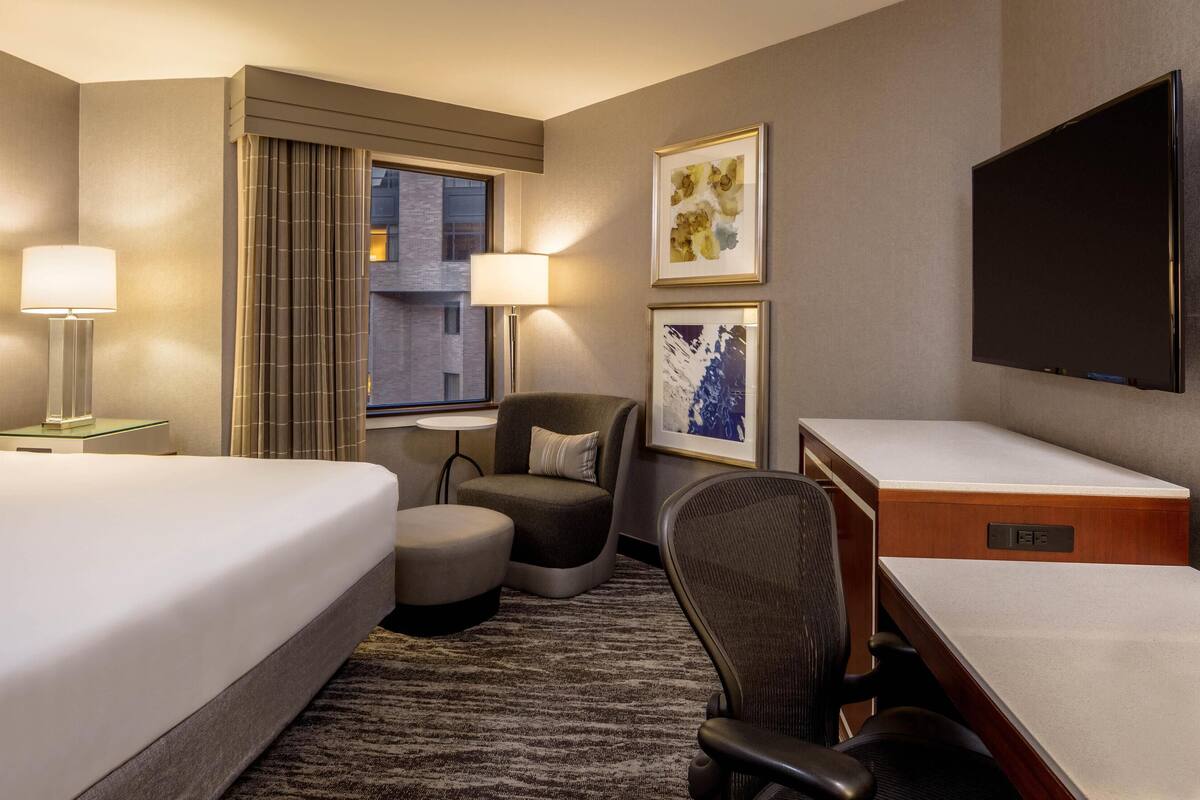 A hotel room with a large bed, a desk, a chair, a TV, and artwork on the walls.