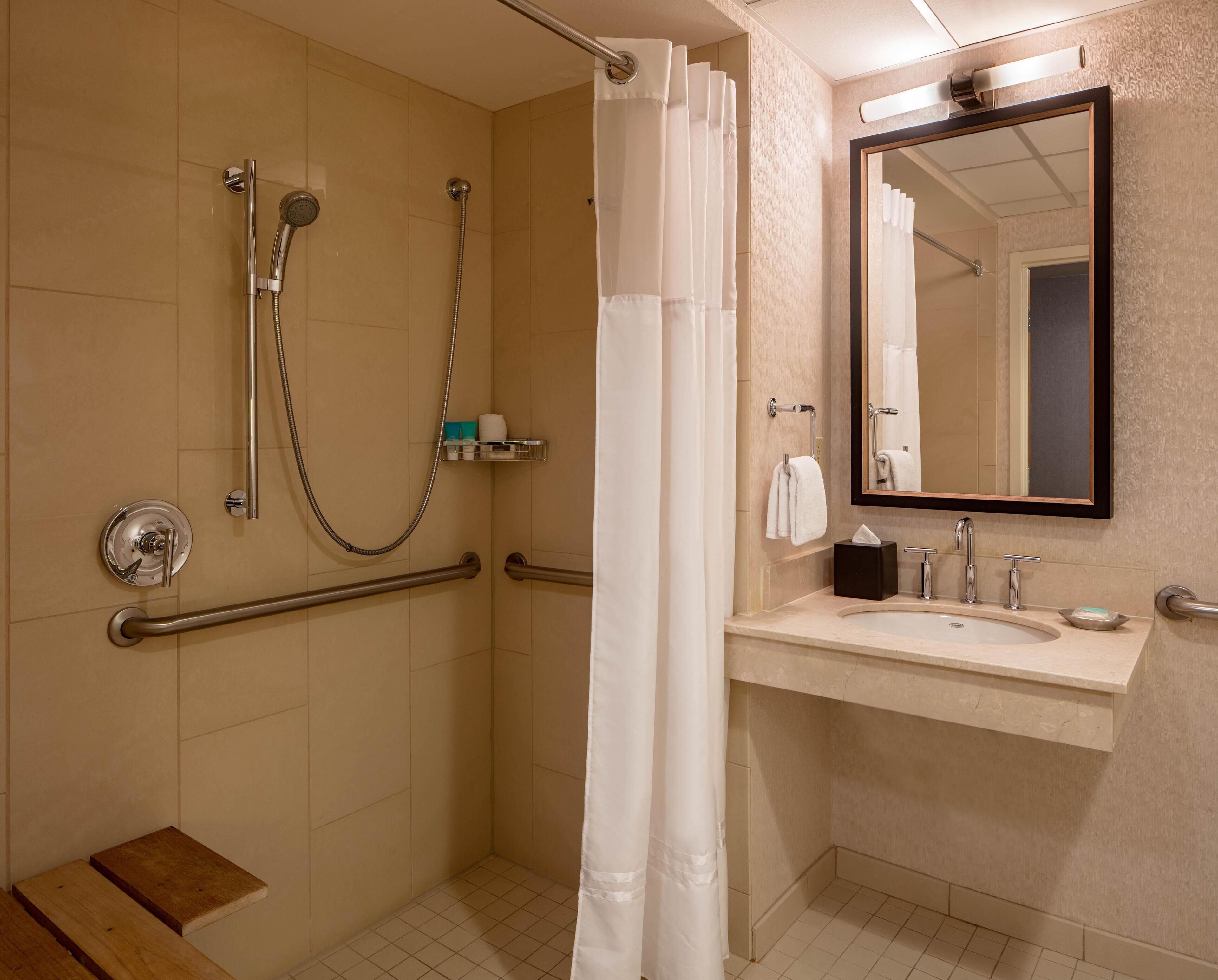 A bathroom with a shower, grab bars, a sink, and a mirror.